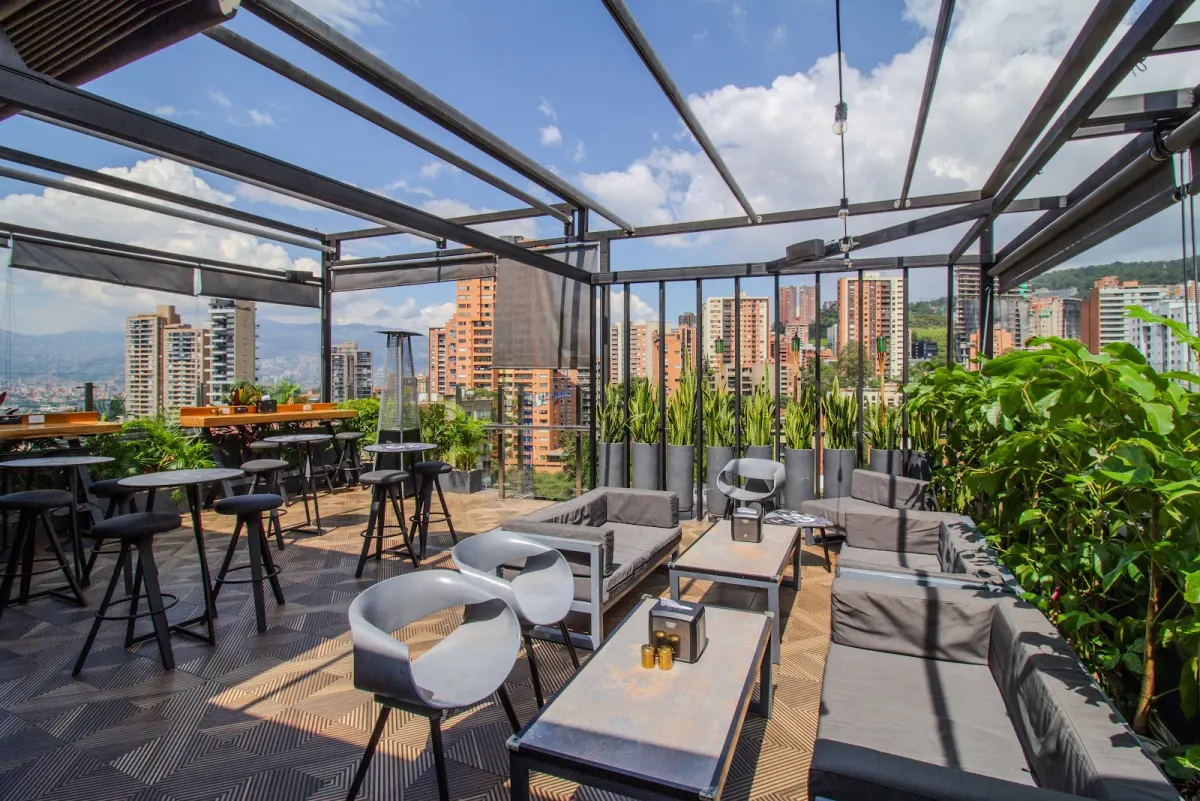The 360 Rooftop terrace at Hotel Haven under an open glass-and-steel frame, with lounge sofas, high tables and planters, and El Poblado's towers behind