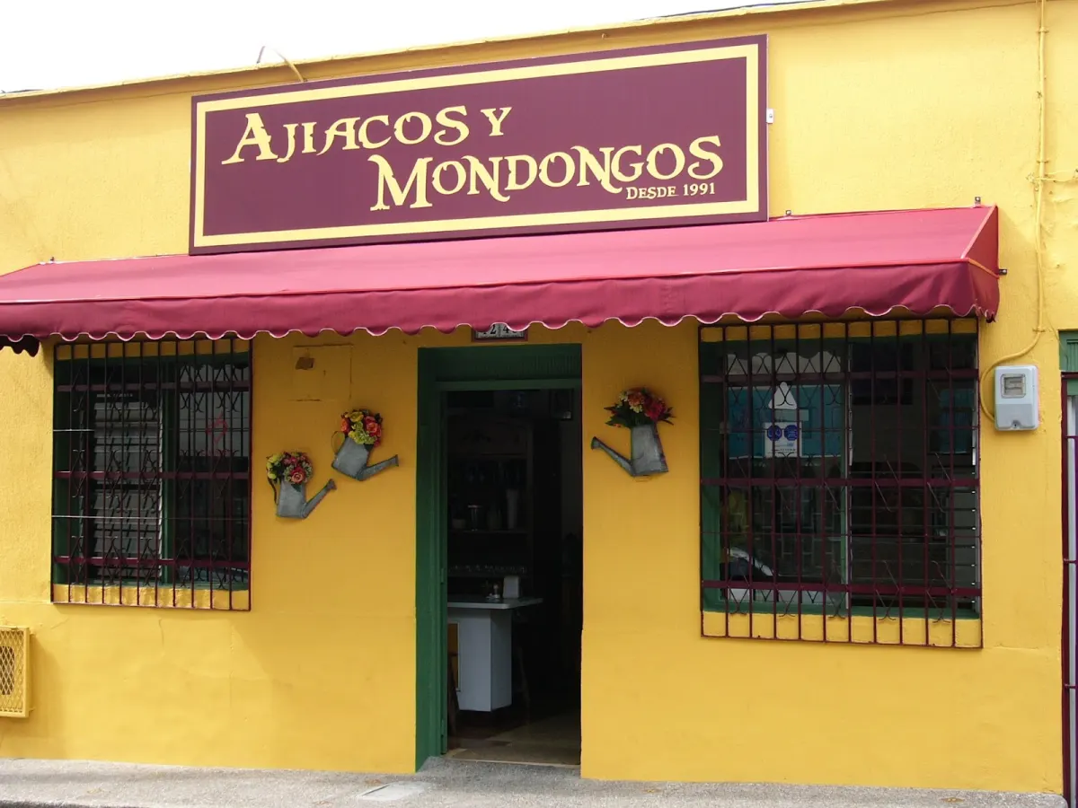 The yellow front of Ajiacos y Mondongos, with a maroon sign reading "Ajiacos y Mondongos desde 1991", a maroon awning and barred windows