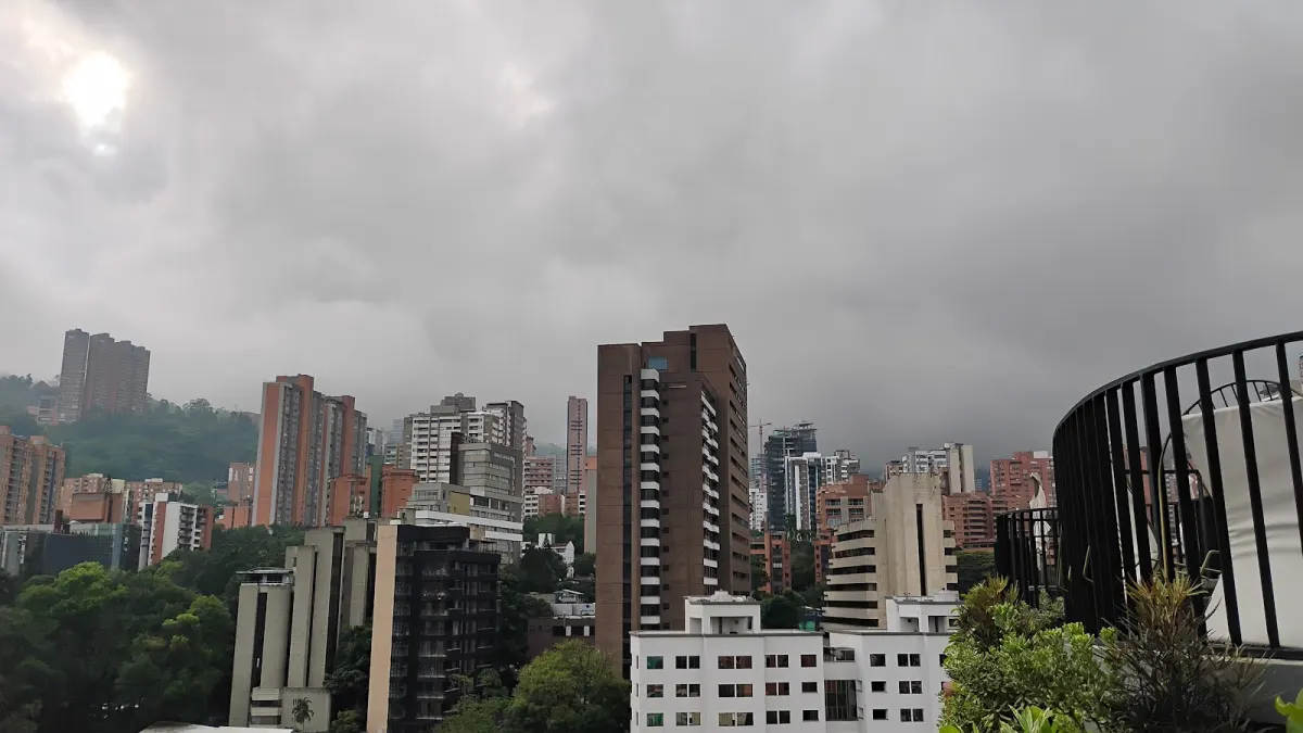 A cloudy view over El Poblado's tower blocks and green hills from Alter's rooftop, with its curved black railing on the right