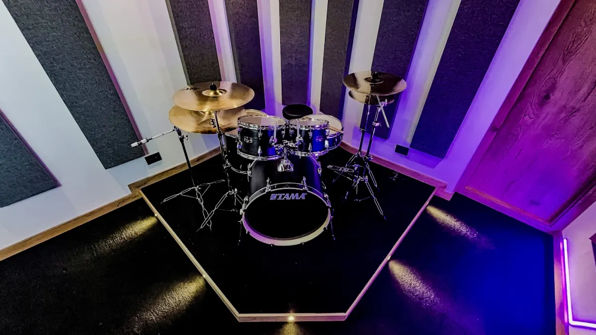 A Tama drum kit on a raised platform in Arketipo Estudio's recording room, between grey acoustic panels on white walls, lit in purple