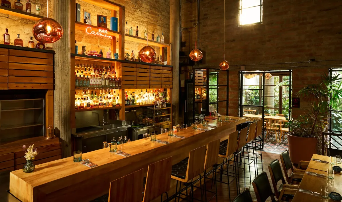 The bar at Carmen, with a long wooden counter and bottles on shelves behind it