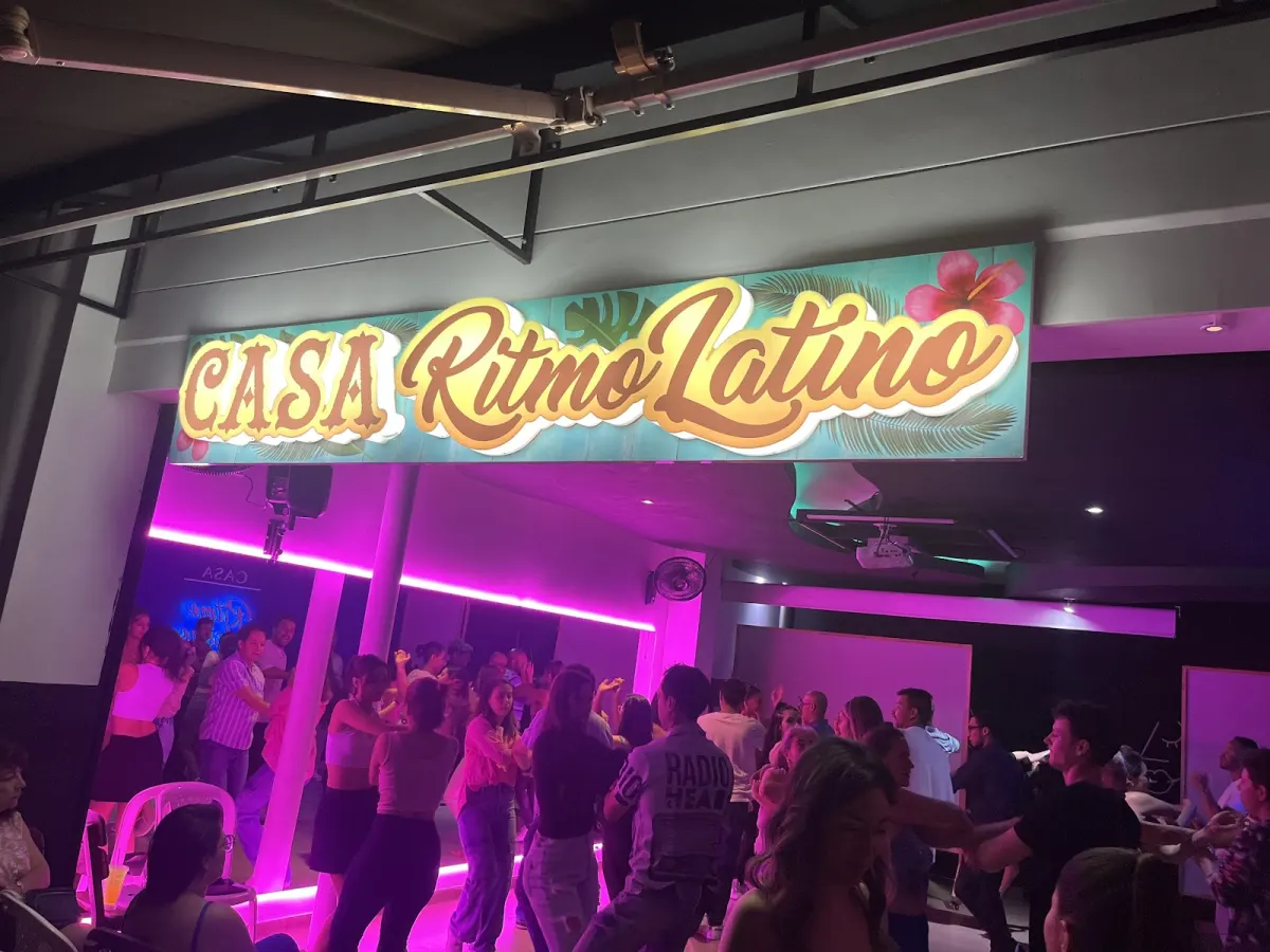 The illuminated Casa Ritmo Latino sign above the studio floor, with dancers below under pink light.