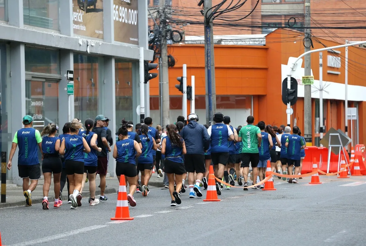 A large group of runners in matching blue INDER shirts jogging away along a coned-off lane of a city street during the Medellín Ciclovía