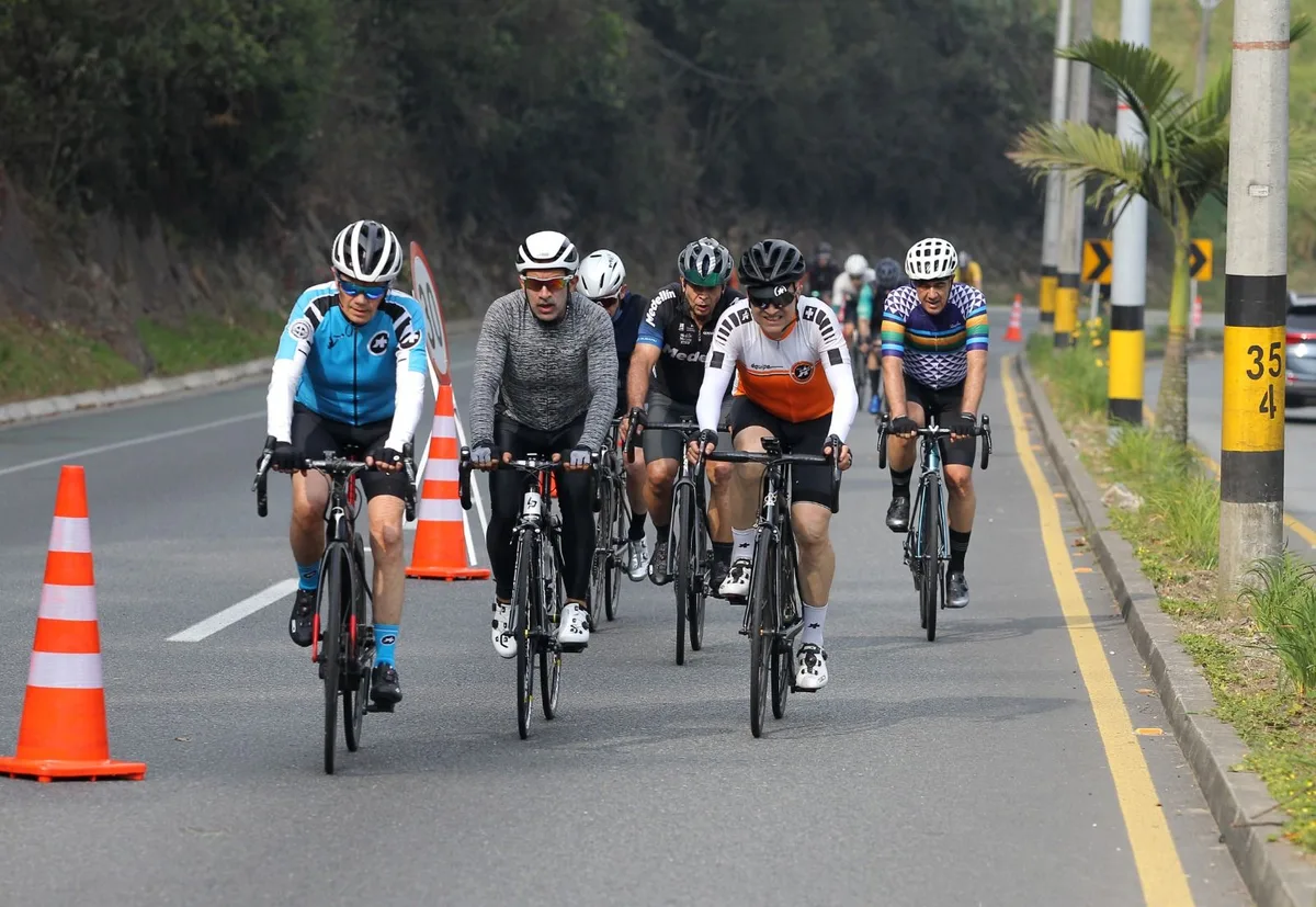 A group of road cyclists in helmets riding up a coned-off lane of Las Palmas on the Medellín Ciclovía, with green hillside behind