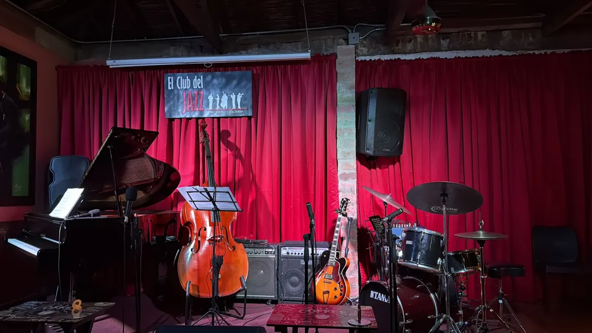El Club del Jazz's stage before a show, with a grand piano, double bass, guitars and a drum kit in front of a red curtain and the club's sign