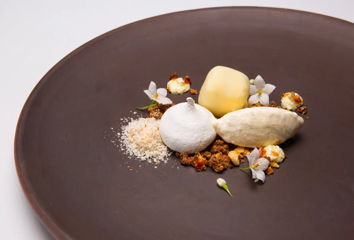A plated dessert decorated with small flowers on a brown plate at Elcielo Medellín