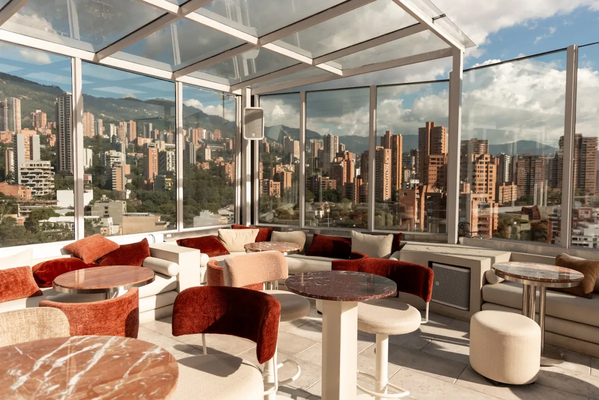 The glass-walled lounge at Envy Rooftop, with terracotta armchairs and marble tables, and El Poblado's towers and hills beyond