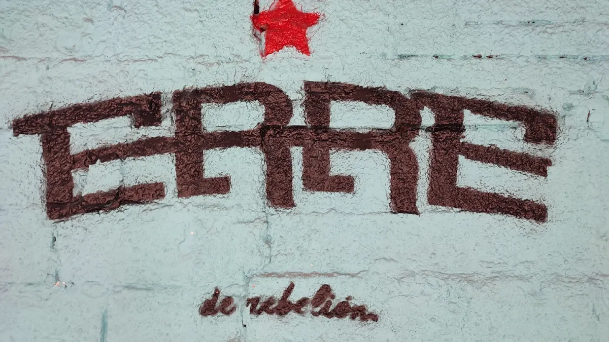 The ERRE logo painted in brown on a pale blue wall under a red star, with 'de rebelión' written beneath