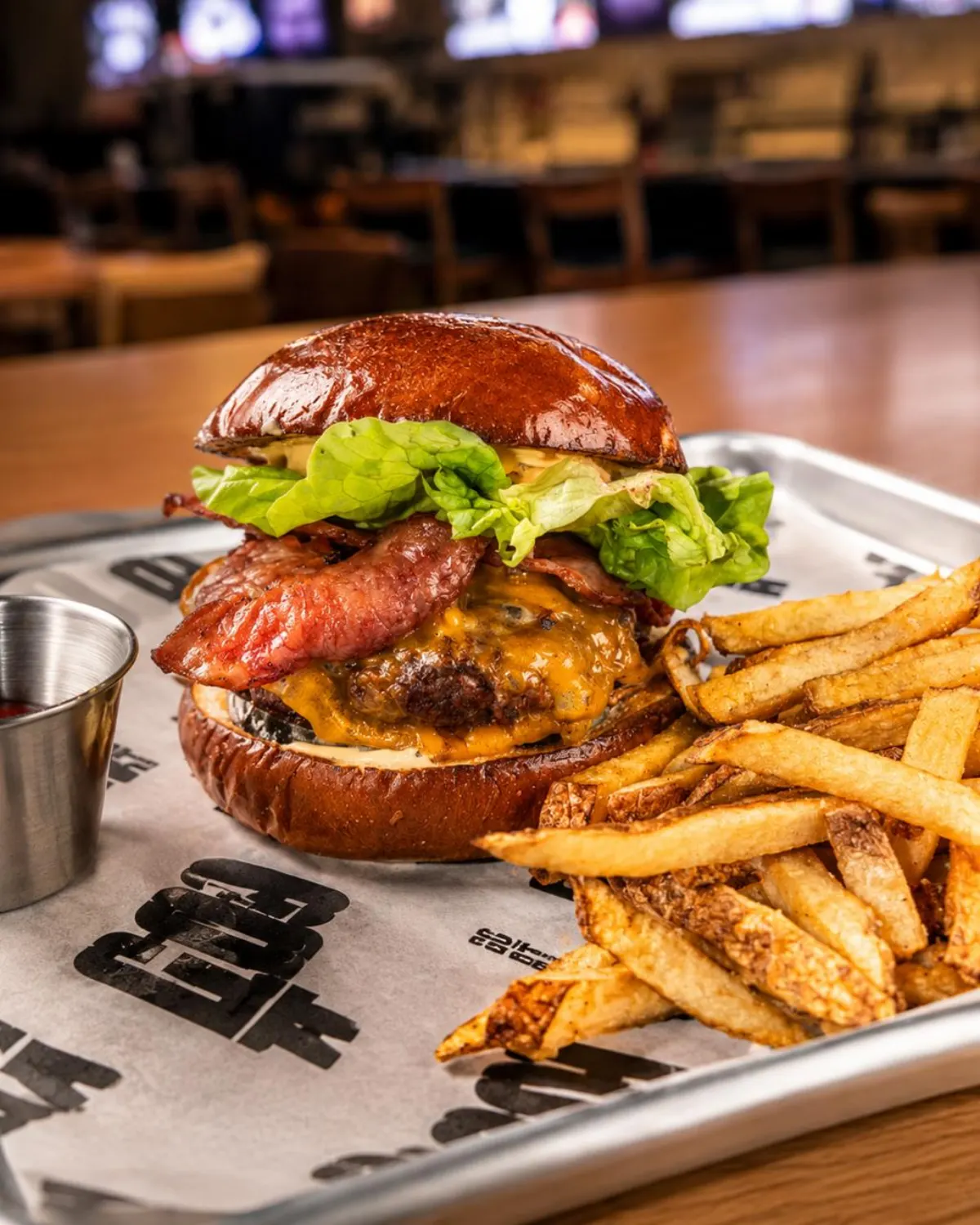 GOAT Sports Bar burger with bacon, melted cheddar and lettuce on a pretzel bun, served with fries on a GOAT-branded tray