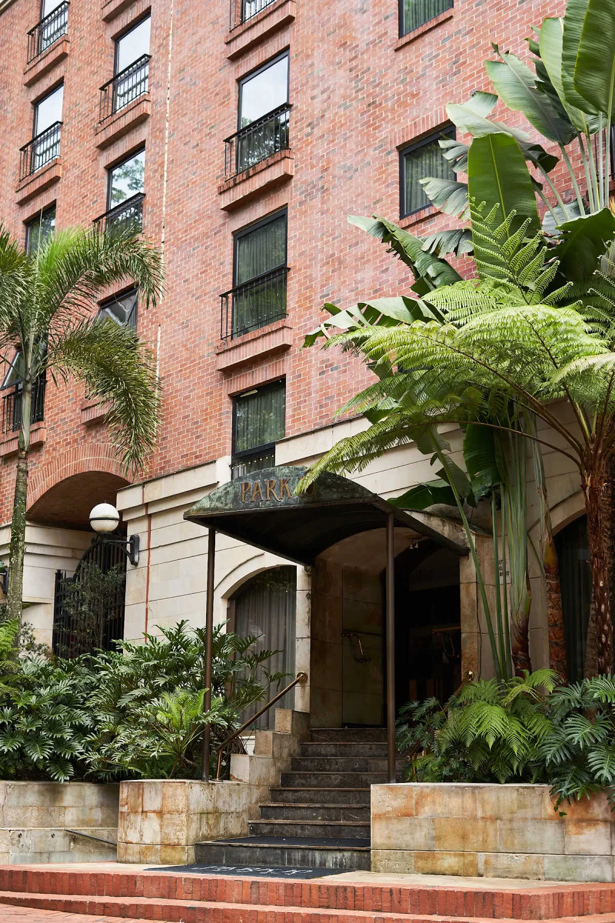 The brick facade and canopied front entrance of Park 10 Hotel in El Poblado, framed by palms and tree ferns