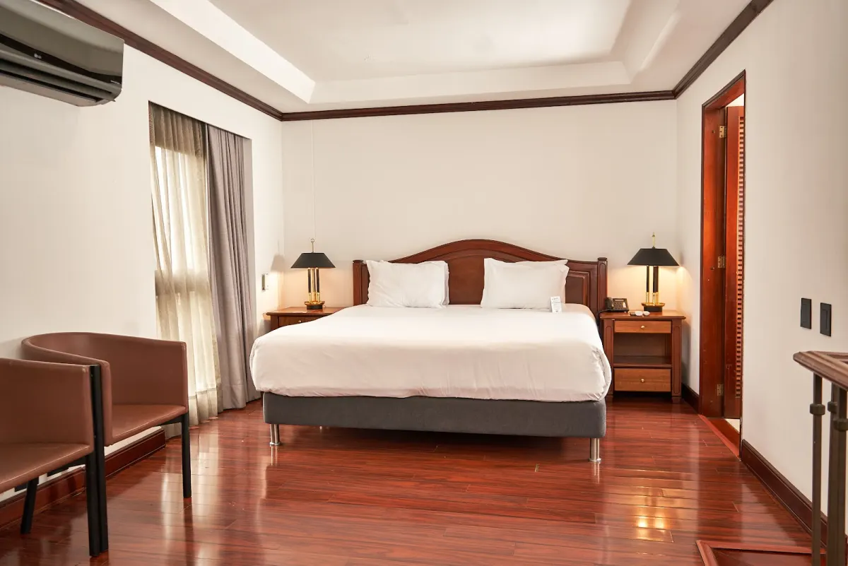 A suite at Park 10 Hotel with a king bed, a dark wood headboard, brass bedside lamps and polished wood floors