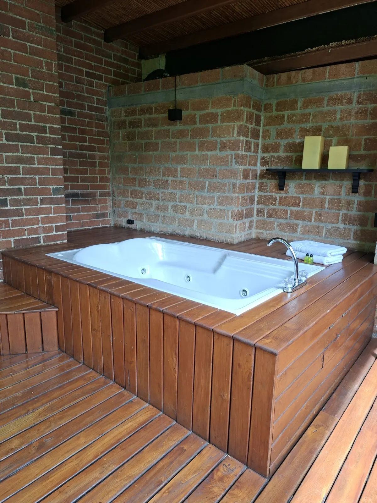 A jetted tub set into a wooden deck against exposed brick walls at Park 10 Hotel