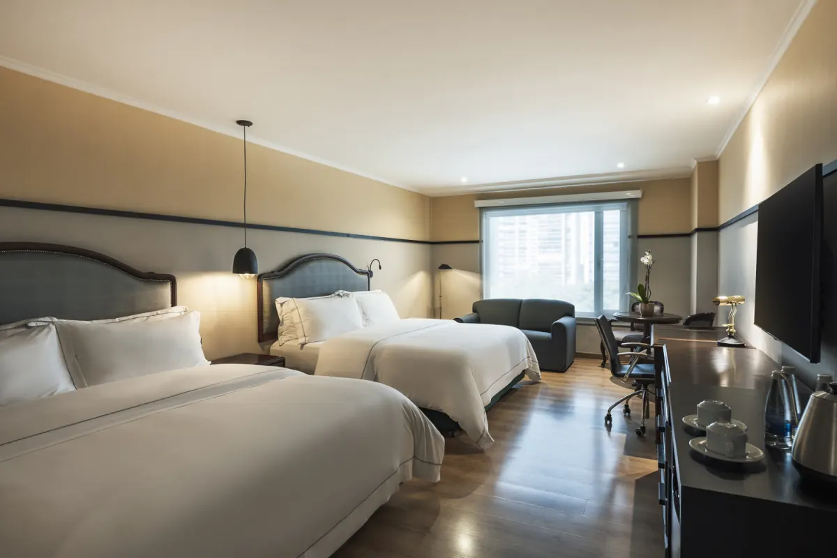 A room at Hotel Poblado Plaza with two double beds, a sofa by the window, a desk and a wall-mounted TV
