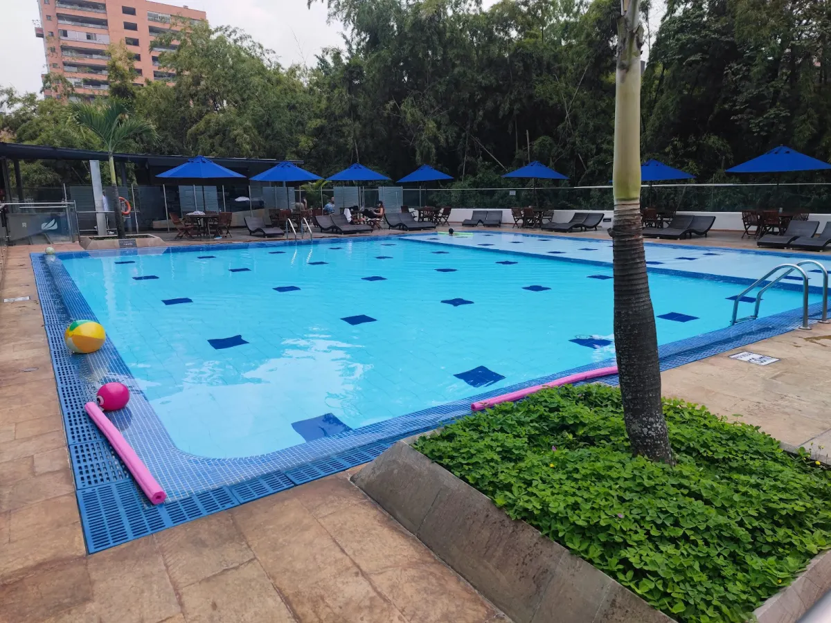 The outdoor pool at Hotel San Fernando Plaza, ringed by loungers and blue umbrellas, with trees behind