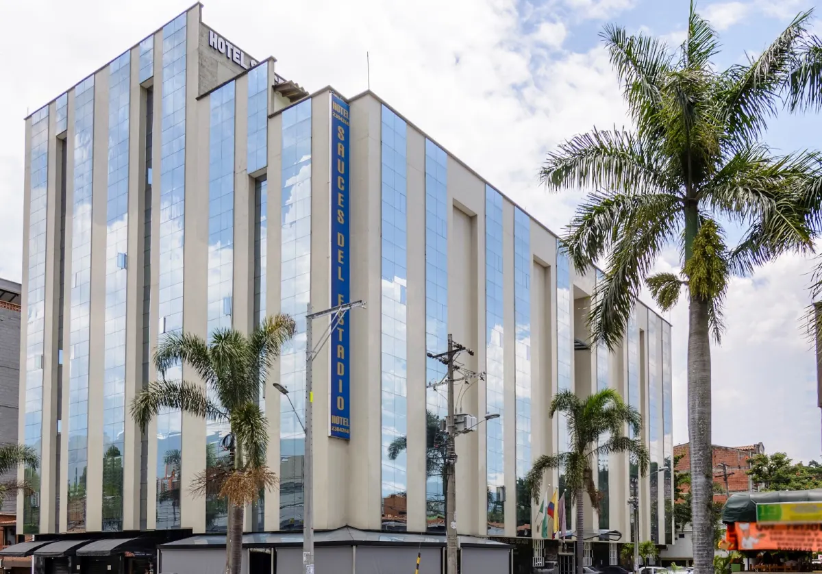The glass-and-cream facade of Hotel Sauces del Estadio, with its vertical blue name sign and palm trees on the street