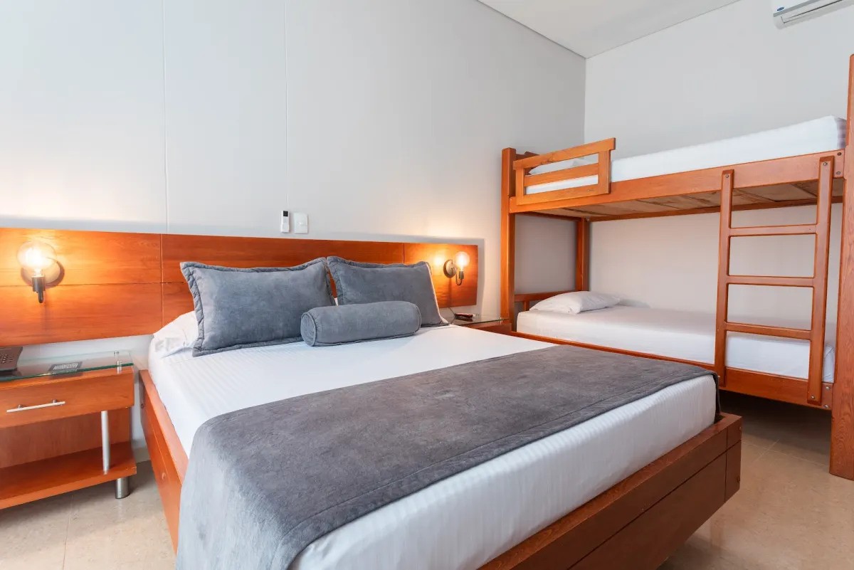 A family room at Hotel Sauces del Estadio with a double bed, a wooden headboard with wall lamps and a bunk bed