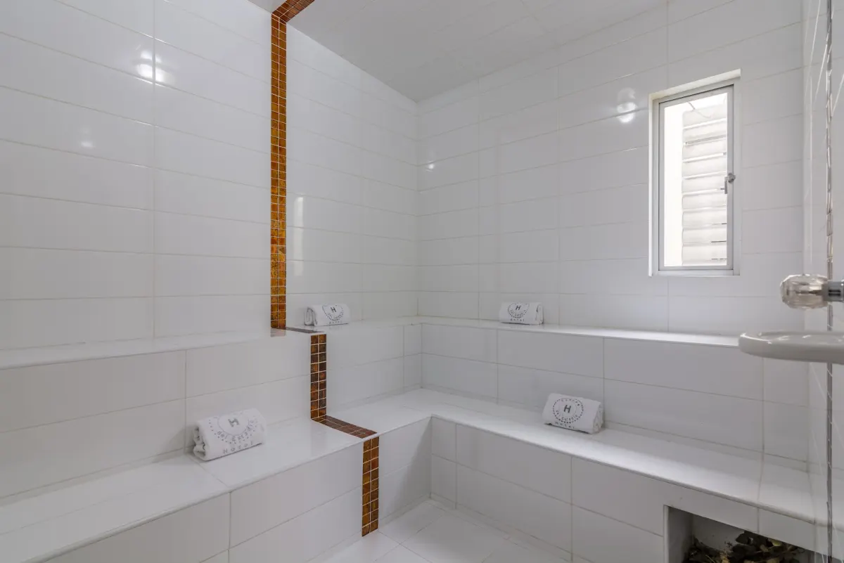 The white-tiled steam room at Hotel Sauces del Estadio, with tiled benches and rolled towels