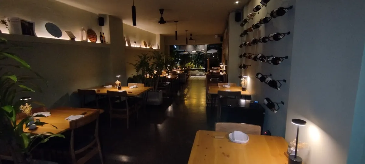 The dimly lit dining room at Restaurante Idílico, with wooden tables, table lamps and wine bottles racked on the right-hand wall