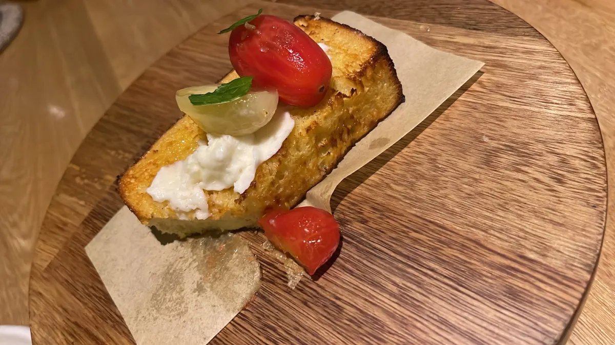 A slice of toasted bread topped with fresh white cheese and tomatoes on a wooden board at Restaurante Idílico