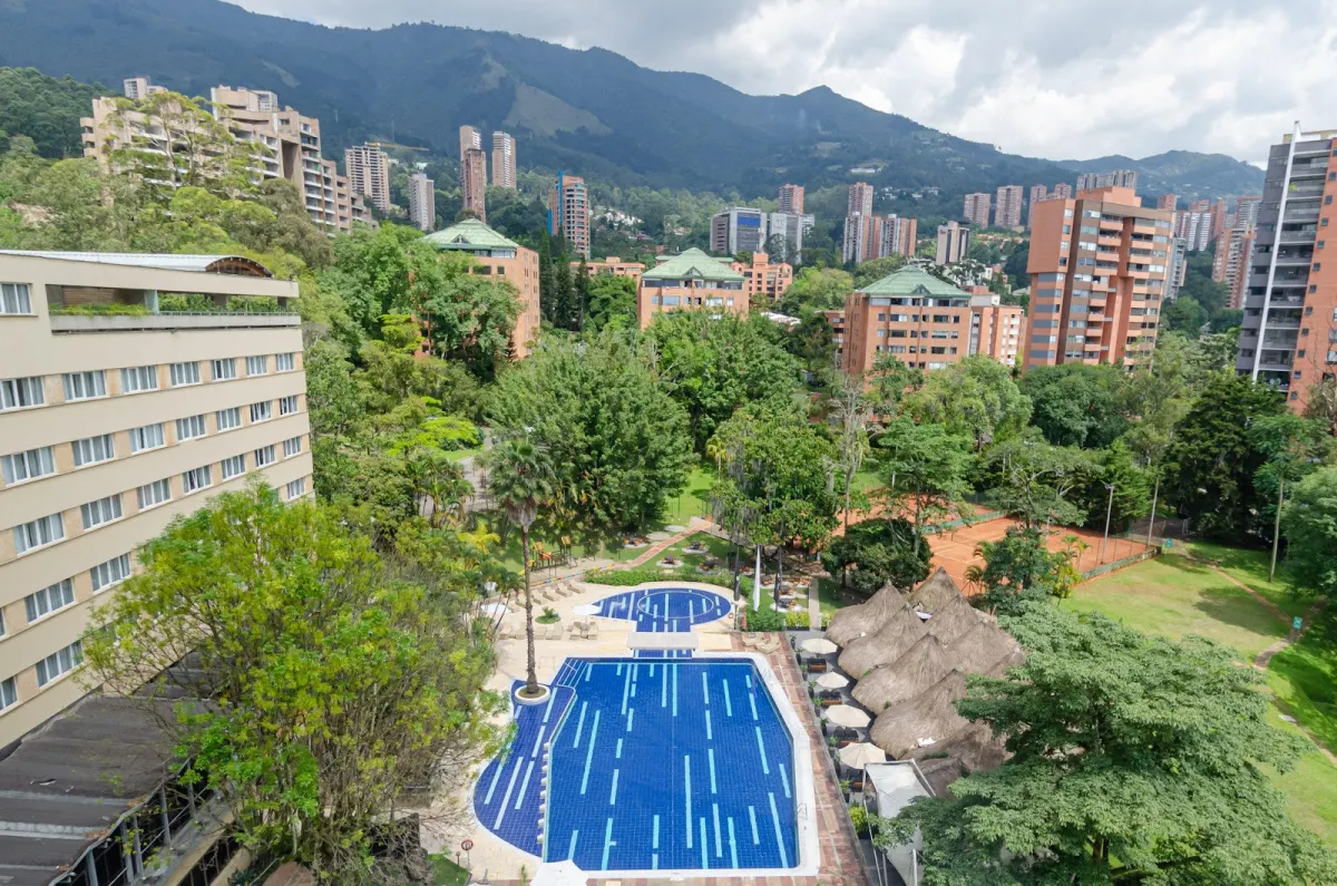 An aerial view of the InterContinental Medellin grounds: the hotel wing, a blue-tiled pool, thatched cabanas, a clay tennis court and the El Poblado hills behind