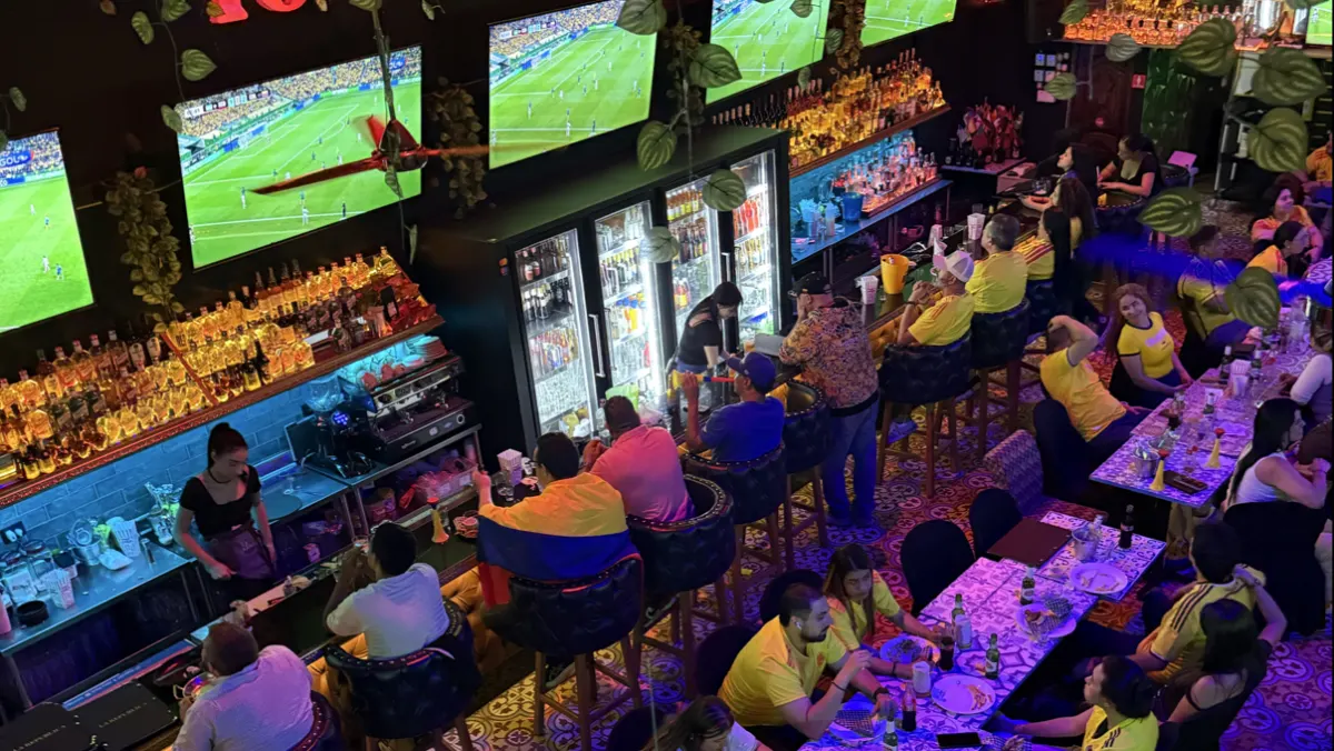 La República Brunch Sport Bar seen from above: fans in Colombia shirts at tables and the bar while several screens show a football match