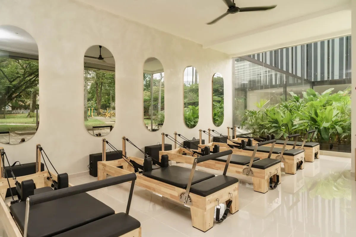 The Laboratorio de Pilates studio in Ciudad del Río, a row of wooden Pilates Reformer machines beneath tall arched mirrors, beside a glass wall onto tropical plants