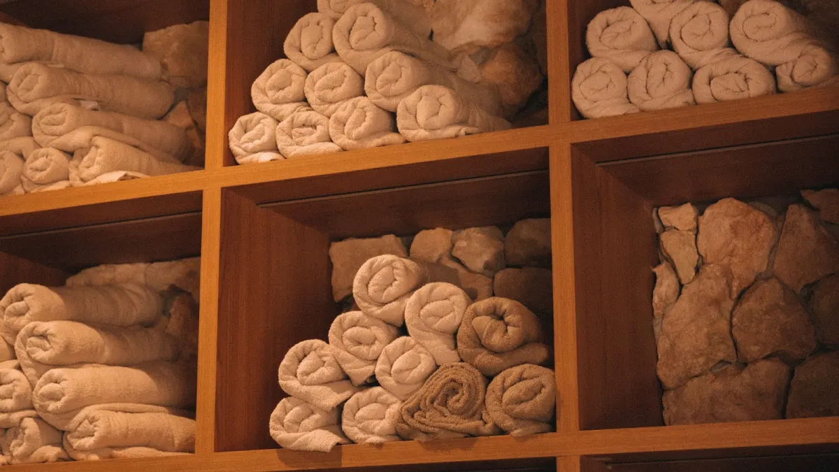 Rolled white and beige towels stacked in wooden cubbies at MADRE, beside a shelf of stacked stones
