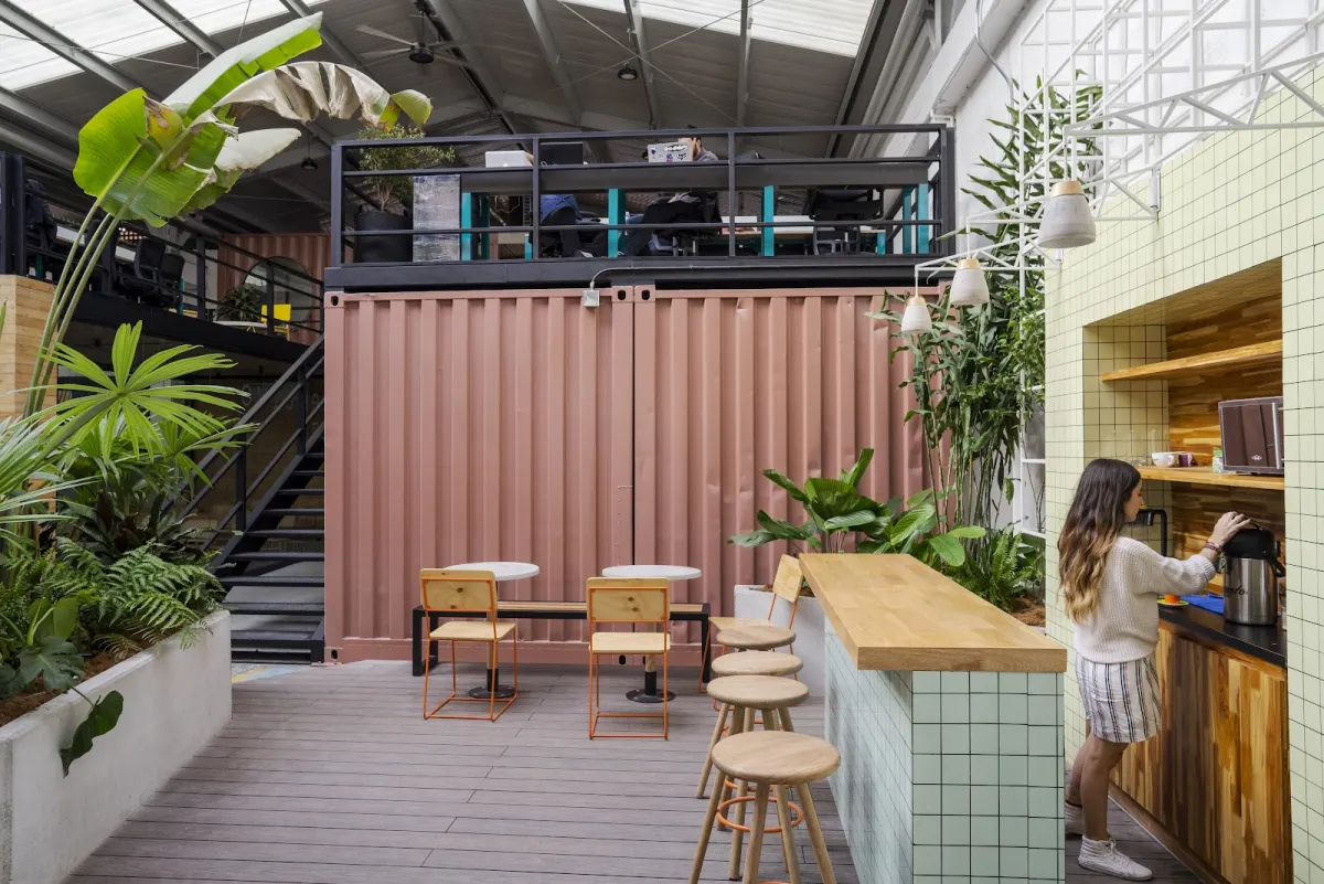 NOI's covered courtyard, with a pink shipping container under a mezzanine of desks, a tiled coffee bar with wooden stools and large tropical plants