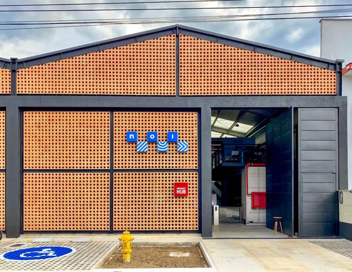 The front of NOI in Ciudad del Río, a perforated orange brick façade with blue NOI lettering and an Impact Hub sign beside the open entrance