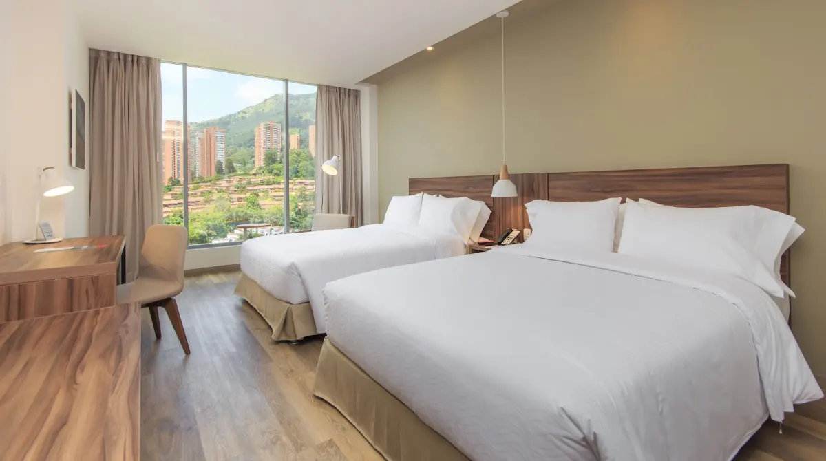 A room at Novotel Medellín El Tesoro with two double beds, a work desk and a floor-to-ceiling window onto El Poblado's towers and hills