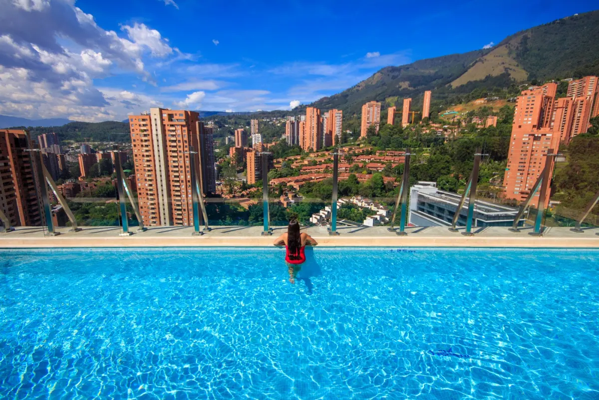 A guest at the edge of the infinity pool at Novotel Medellín El Tesoro, looking out over brick tower blocks and the mountains