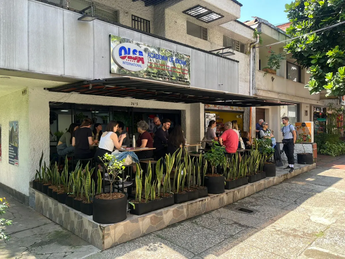 The front of OLSA International, with its "OLSA International Academia de Idiomas" sign above a covered terrace where students sit at high tables behind a row of potted plants