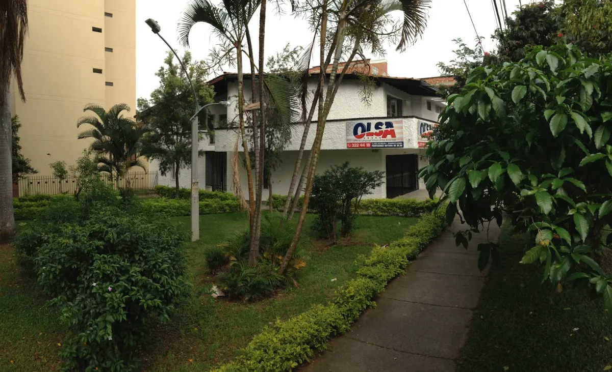 An older view of OLSA International in a white two-storey house with an OLSA banner on the balcony, set behind a lawn, palms and a garden path
