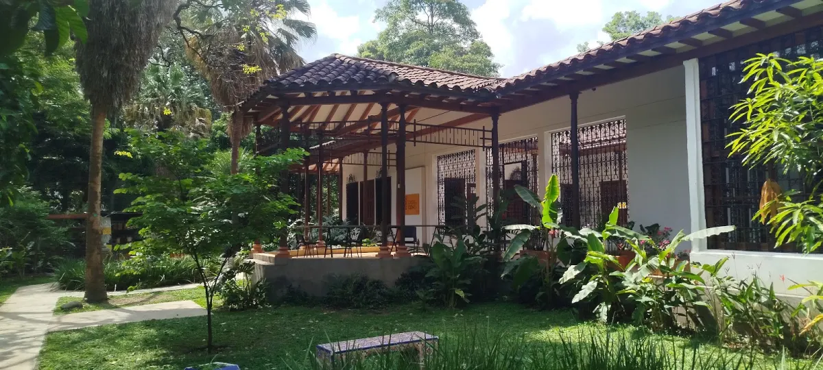 A white colonial-style house with a tiled roof and wooden balcony among tropical plants and palms in the Parque de la Conservación