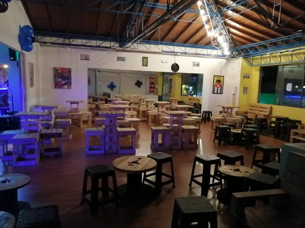 The lounge side of Químbara Cumbara's studio, with pallet-wood tables and stools under a high timber roof.