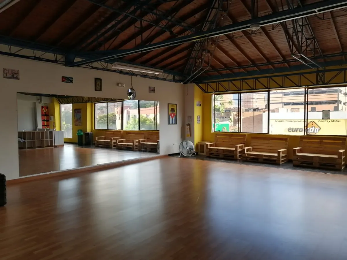 Químbara Cumbara's empty dance studio, with a wooden floor, a wall of mirrors and pallet-wood benches under the windows.