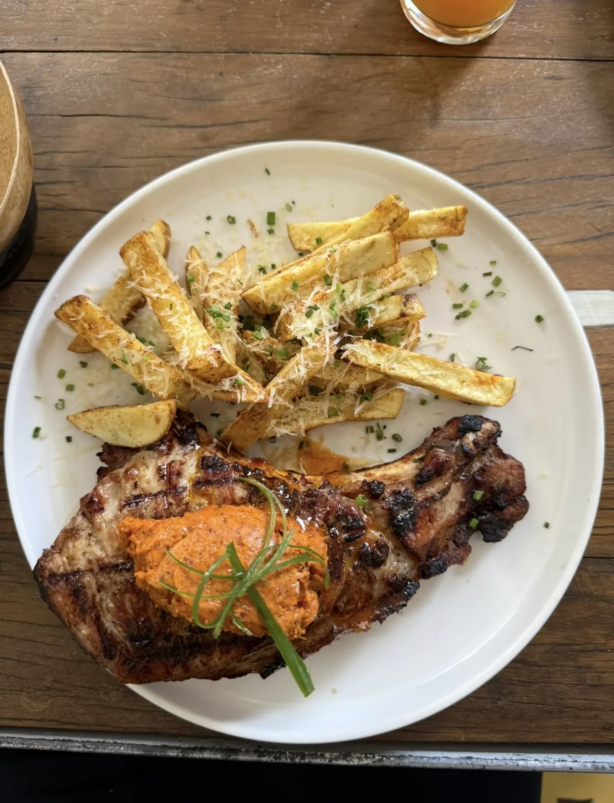 A grilled pork chop topped with an orange butter and chives, with parmesan-dusted potato wedges, on a white plate at Salón Centro