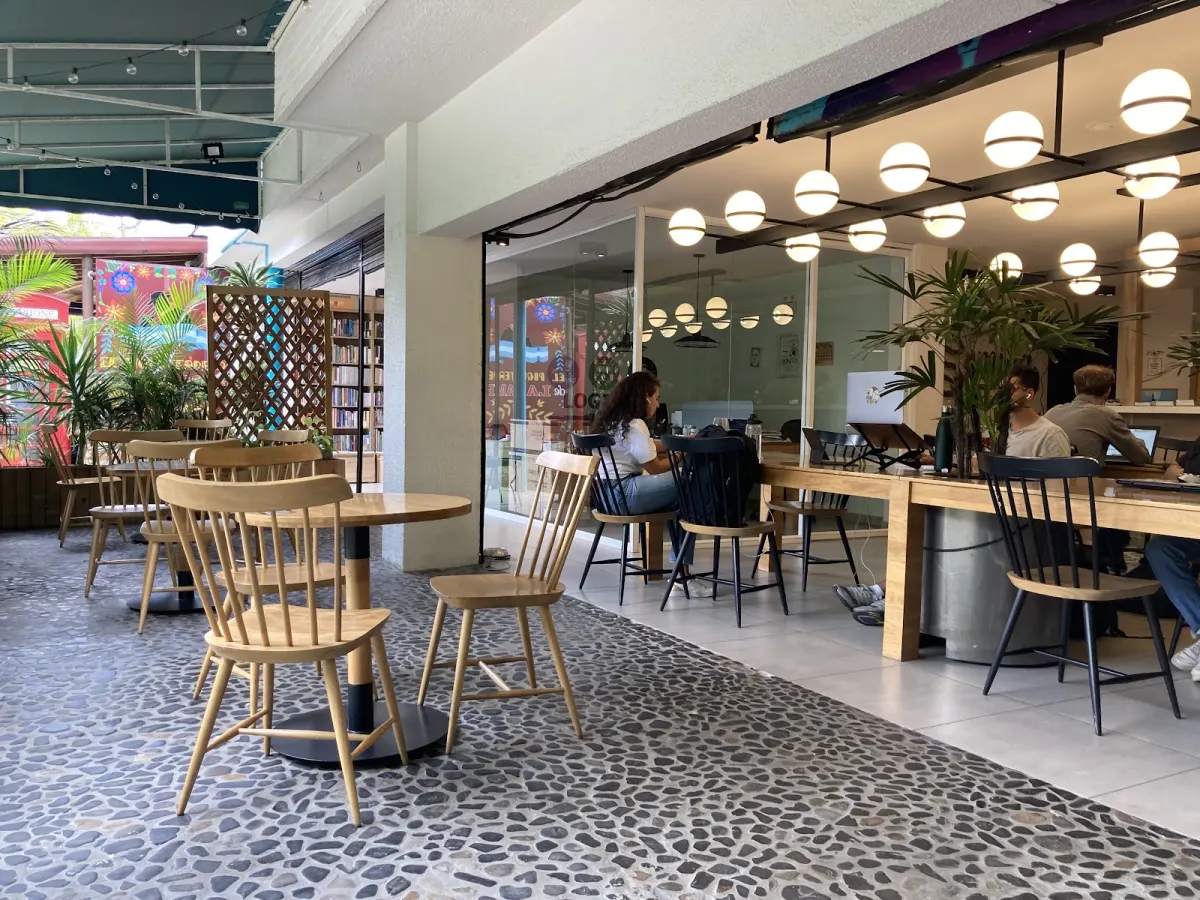 Semilla's café, with wooden chairs and tables on a pebbled floor outside and people working on laptops at a long table under globe lamps inside
