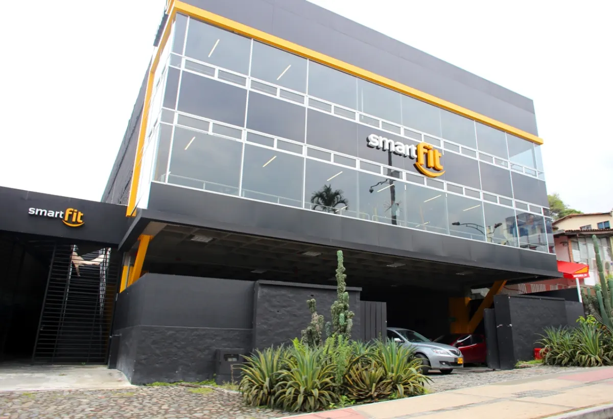 The outside of Smart Fit La 10, a glass-fronted building with the yellow Smart Fit sign above the entrance and car park
