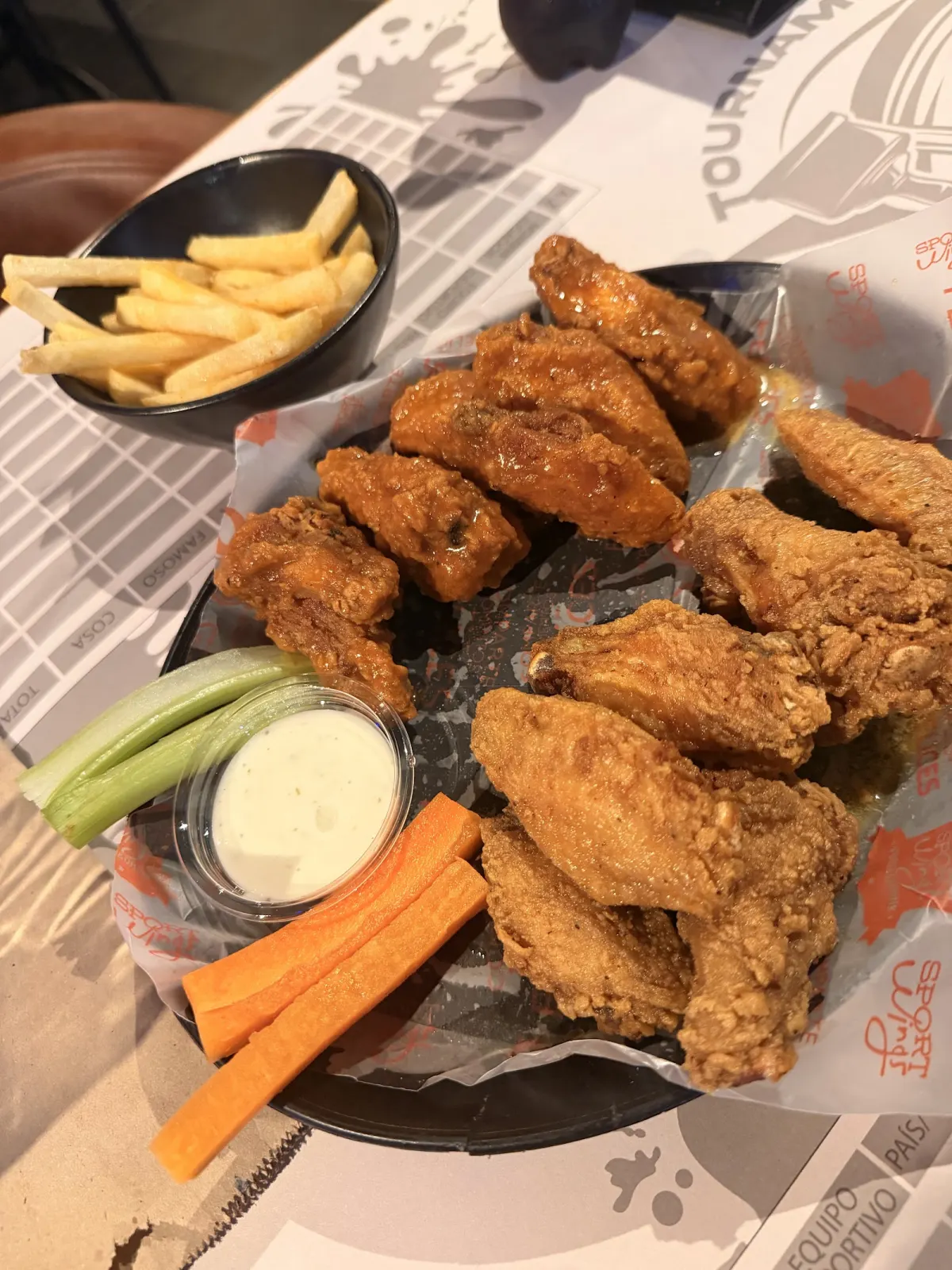 Basket of fried and sauced chicken wings with carrot and celery sticks, ranch dip and a bowl of fries at Sport Wings Laureles