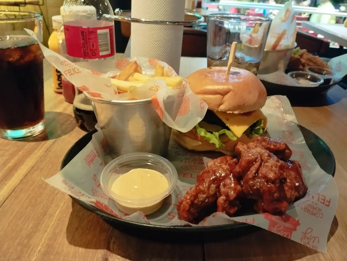 Cheeseburger, saucy wings and fries in a metal cup with dipping sauce on Sport Wings-branded paper at Sport Wings Laureles