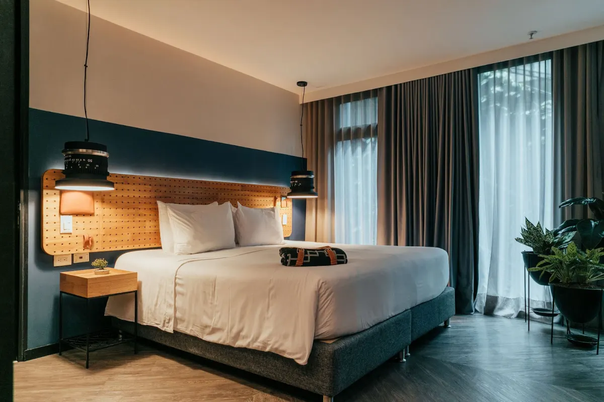 A guest room at The Click Clack Hotel Medellín with a king bed, a pegboard headboard, pendant lamps and floor-length curtains